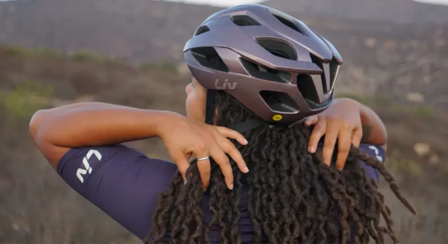 Donna con dreadlocks che regola un casco da bici Liv. Non preoccuparti se il tuo casco è stretto, ci sono modi per allargare il casco stretto.