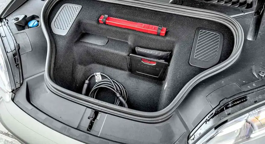 Otwarty bagażnik Porsche Macan z kablem do ładowania, apteczką i instrukcją.