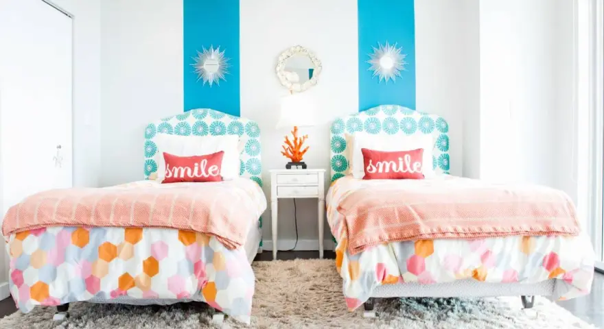 Dos camas gemelas en habitación pequeña, con cabeceros estampados y colchas naranjas. ¡Una solución genial para como poner dos camas en una habitacion pequeña!