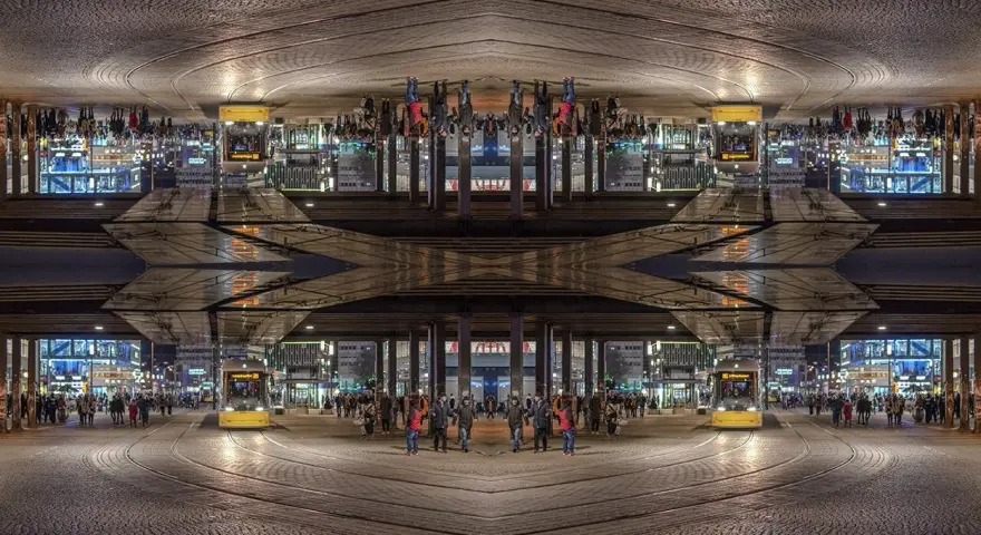 Nocne miasto z żółtym tramwajem i ludźmi. Kompozycja symetryczna tworzy surrealistyczny, odbity świat.