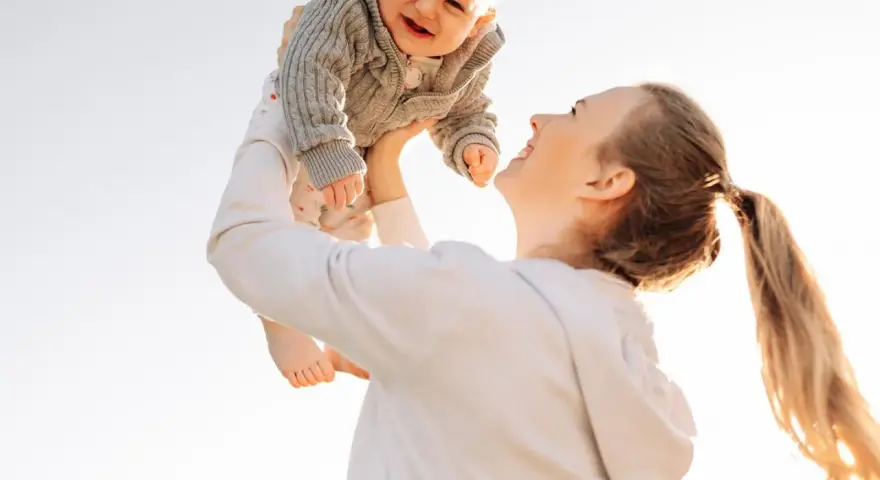 Mutter wirft ihr lachendes Baby in die Luft. Ein fröhlicher helikopter-mutter test im Freien.