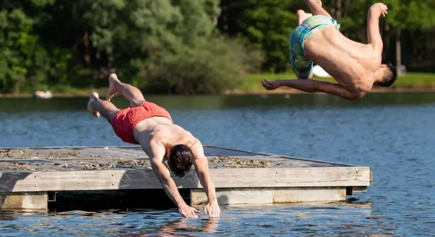 Zwei Männer springen vom Steg in den Sieglarer See. Einer macht einen Salto, der andere taucht gerade ins Wasser.