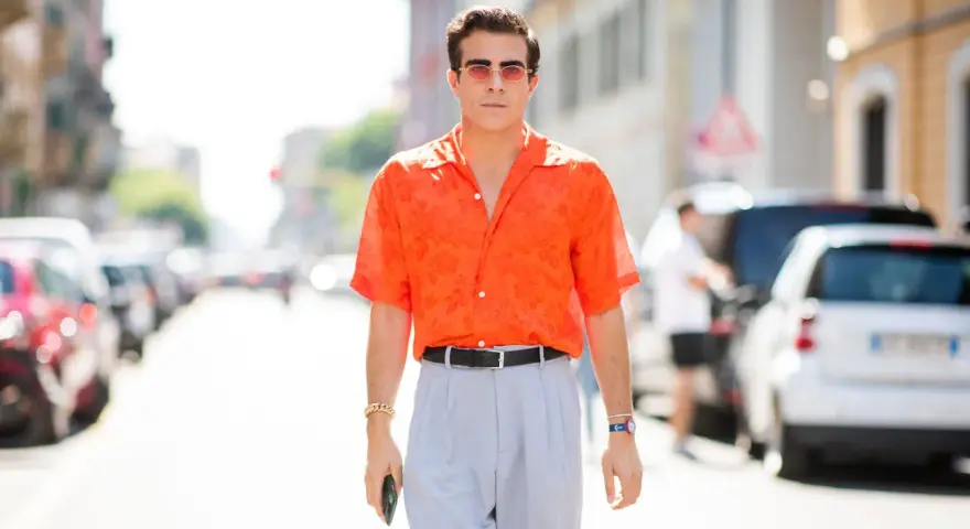 Hombre con camisa naranja estampada y pantalones grises, luciendo un elegante french tuck.