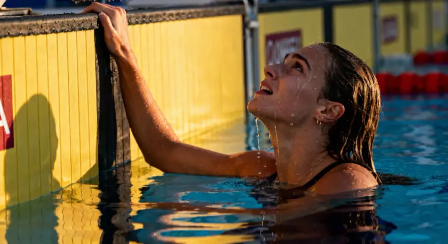 Nuotatrice con gocce d'acqua sul viso, aggrappata al bordo giallo della piscina. Si può fare il bagno in piscina con il ciclo, senza problemi.