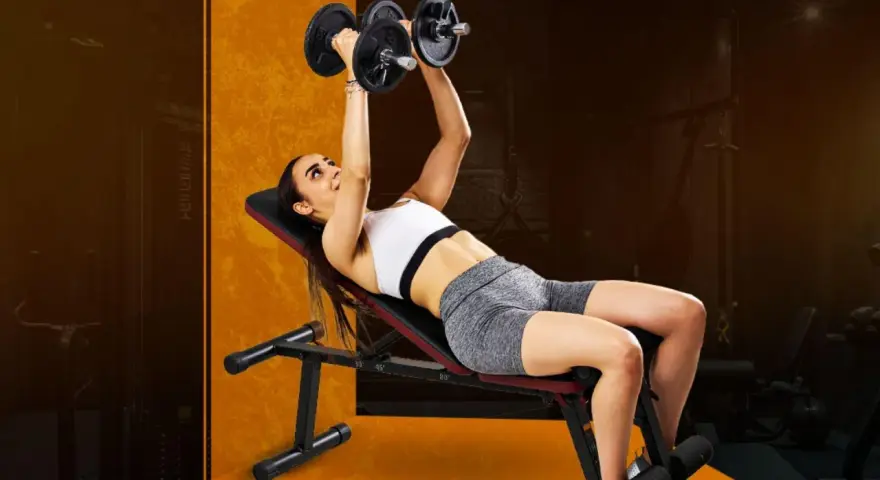 Kvinna utför lutande hantelpress på träningsbänk i gym.