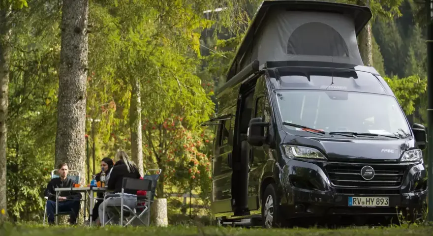 En solig dag med en clever sunny 540 husbil parkerad i skogen. Tre personer sitter vid ett bord och njuter av naturen.