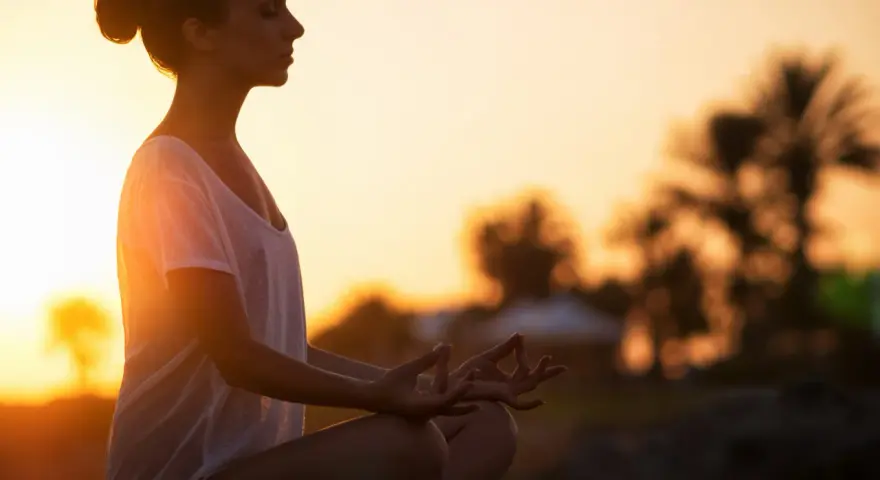 Frau meditiert im Sonnenuntergang. Ein kurzer 5-Minuten-Meditations-Text könnte hier perfekt passen, um diese friedliche Szene zu vertiefen.