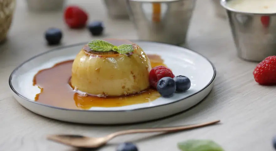 Delicioso flan de queso con caramelo, adornado con menta y frutos rojos.