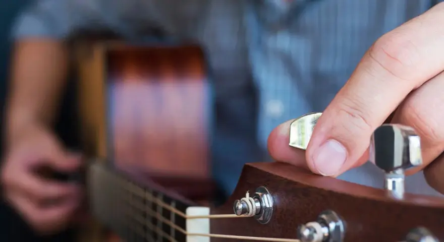 Dłoń stroi gitarę, kręcąc kluczem, by uzyskać idealny dźwięk E.