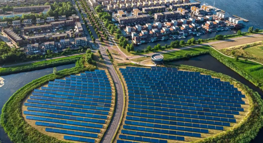 Un grande campo di pannelli solari, simbolo di rigenerazione urbana significato, circonda un quartiere residenziale con case moderne e canali.