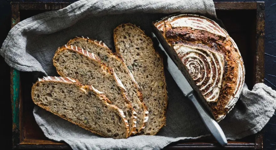 Ein rustikales Roggenbrot, in Scheiben geschnitten, liegt in einer Holzkiste auf Leinentuch. So vielseitig, was man aus Roggen machen kann!