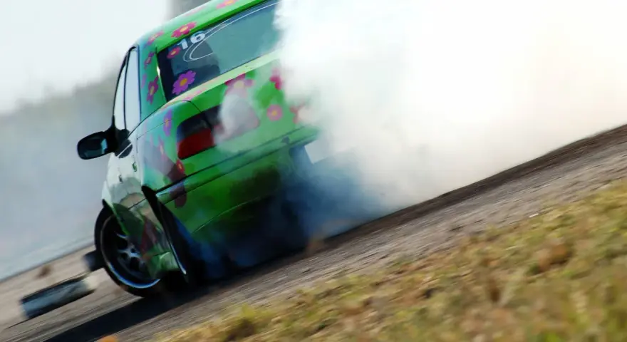 Zielony samochód z kwiatami driftuje, wydzielając dużo dymu.