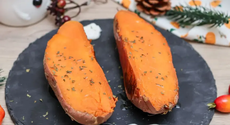 Dos mitades de boniato al horno, tiernas y doradas, con hierbas picadas y una cucharada de crema.