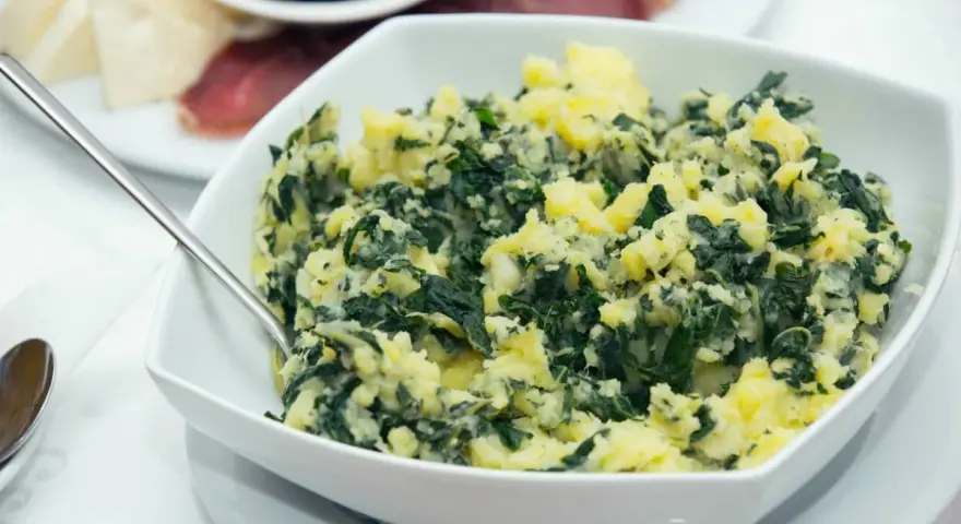 Un tazón blanco lleno de acelgas con patatas, un plato casero y reconfortante.