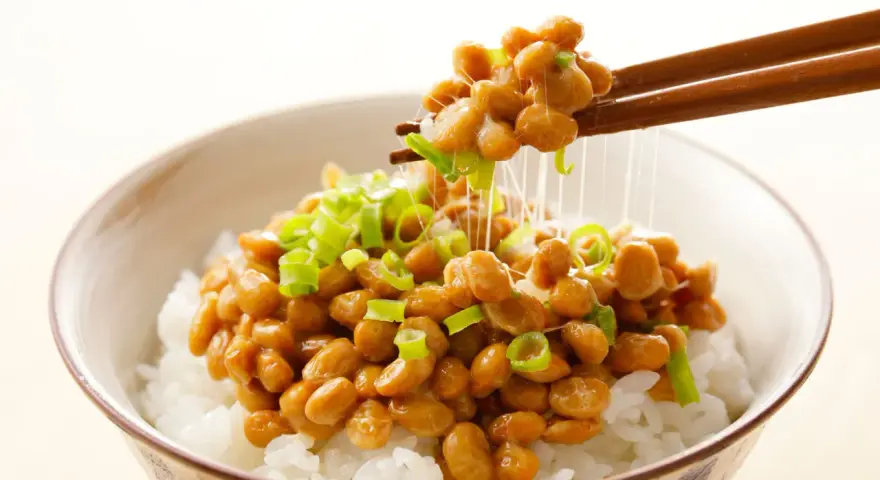 Miseczka ryżu z natto, japońską potrawą z fermentowanej soi, posypana szczypiorkiem. Pałeczki unoszą nitki natto.