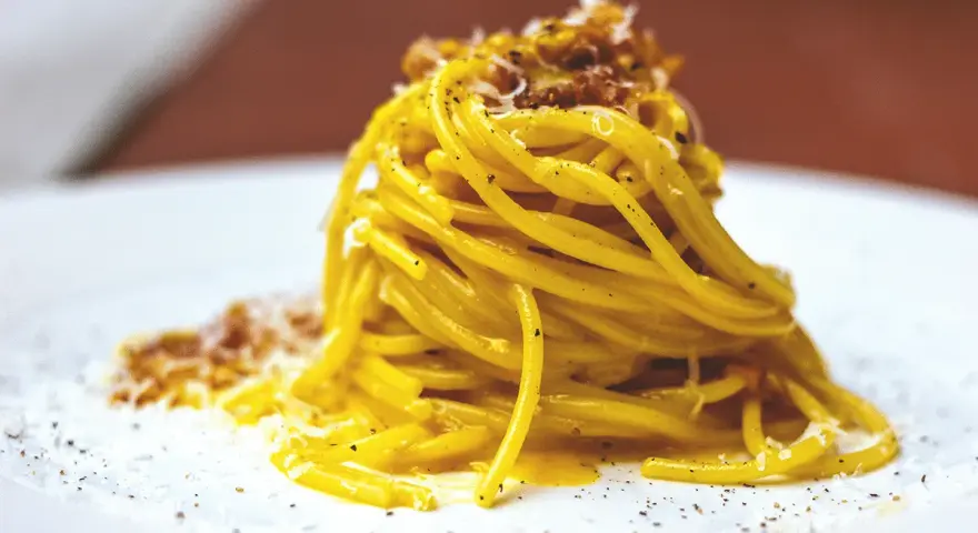 Un piatto di spaghetti alla carbonara fumante, guarnito con pecorino e pepe nero.