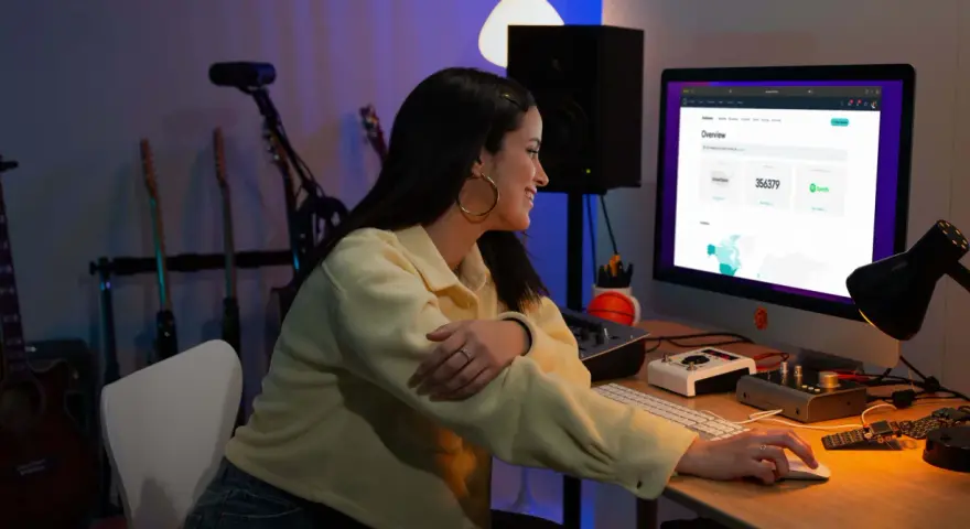 Junge Frau am Computer, die Statistiken für digitalen Musikvertrieb prüft. Gitarren im Hintergrund.