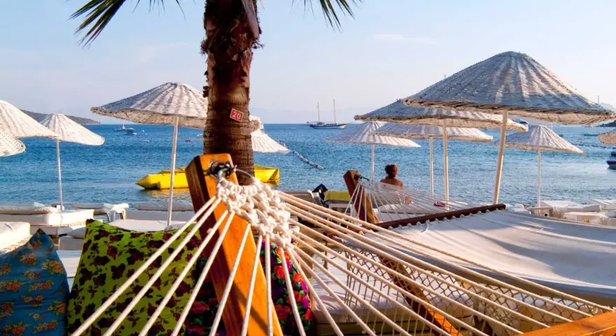 Hamaki i parasole na plaży w Turcji z widokiem na morze i żaglówki.