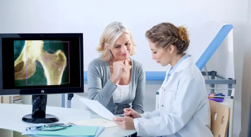 Lekarka omawia z pacjentką wyniki badania RTG stawu biodrowego, wskazując na objawy osteoporozy.