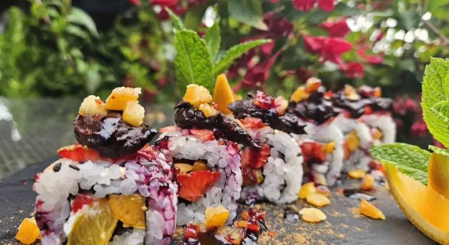 Roladki sushi z owocami, posypane cukrem pudrem i udekorowane miętą i pomarańczą.