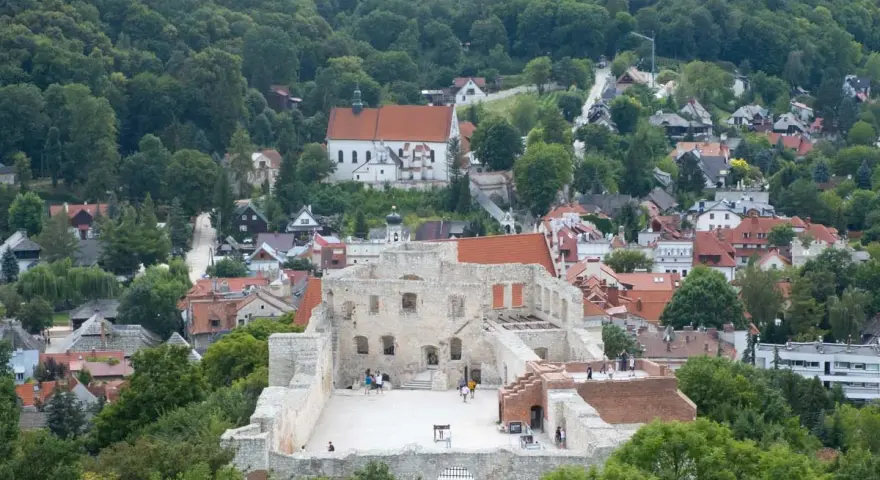 Ruiny zamku w Kazimierzu Dolnym na tle zielonych wzgórz i zabudowań.