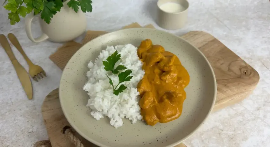 Pyszny Butter Chicken przepis na talerzu z ryżem i natką pietruszki. Idealny obiad.