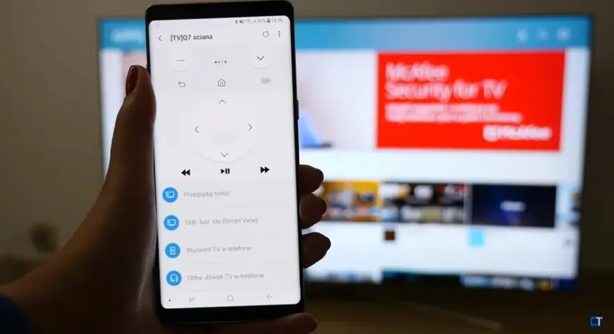 Smartfon z aplikacją do sterowania TV, umożliwiający screen mirroring. Na ekranie telefonu widoczny pilot, a na telewizorze reklama McAfee.