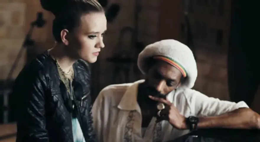 Snoop Dogg w białej koszuli i beretce Rasta, rozmawiający z młodą kobietą. Może to być scena z jednego z jego **snoop dogg utworów**.