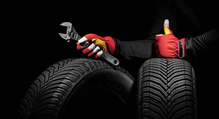 Mani guantate con chiave inglese e pollice in su, su pneumatici. Il significato dei pneumatici è affidabilità e sicurezza.