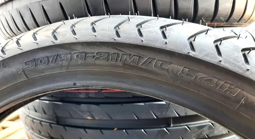 Opona motocyklowa z oznaczeniem 90/90-21M/C 54H. Szerokość opony jest kluczowa dla przyczepności.