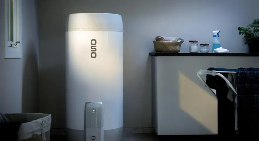 En OSO smart varmvattenberedare står i ett tvättstuga. Bredvid finns en tvättkorg och en torkställning med kläder.
