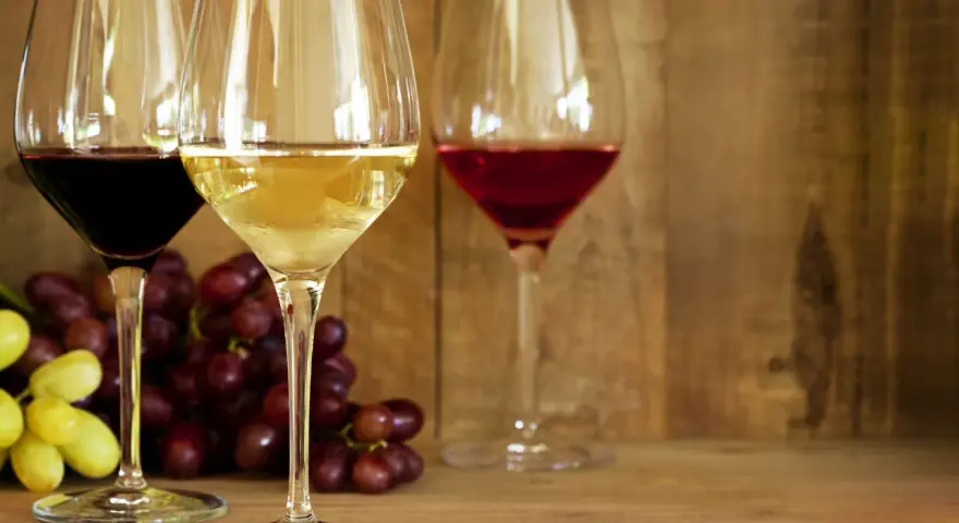 Trzy kieliszki z winem: czerwonym, białym i różowym, obok kiście winogron. Idealne na prosty przepis na wino.