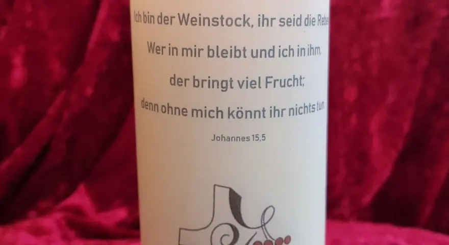 Der Text auf der Kerze zitiert Johannes 15,5: "Ich bin der Weinstock, ihr seid die Rebe. Wer in mir bleibt und ich in ihm, der bringt viel Frucht; denn ohne mich könnt ihr nichts tun.