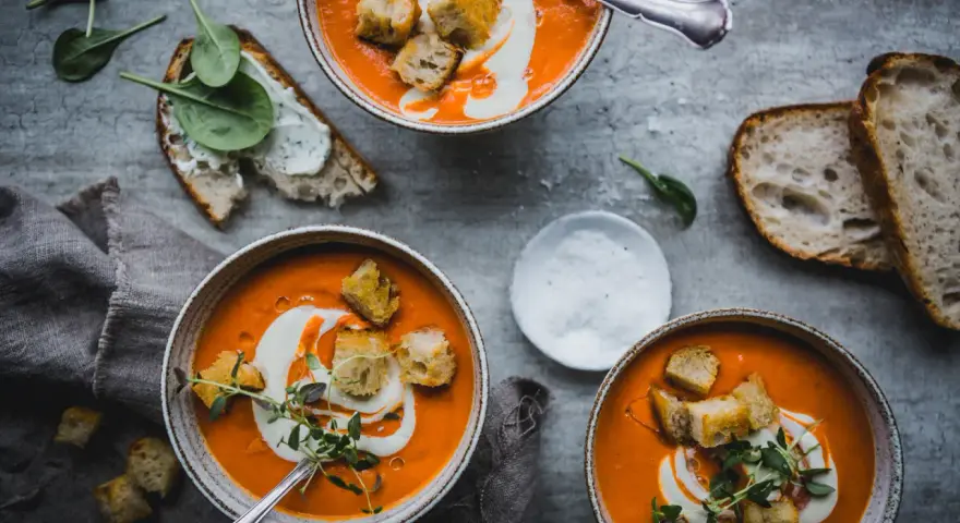 Tre skålar med krämig tomatsoppa, toppad med krutonger och en virvel av grädde. Perfekt för ett mysigt tomatsoppa recept.