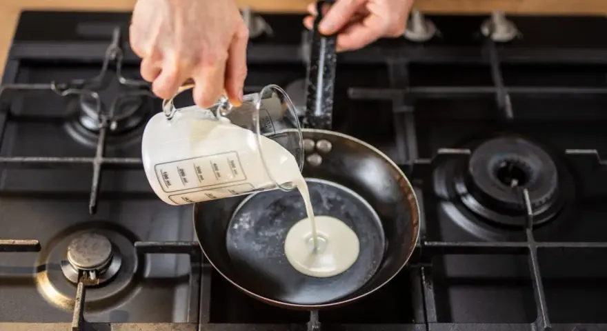 Mani versano panna da cucina in una padella su un fornello a gas.