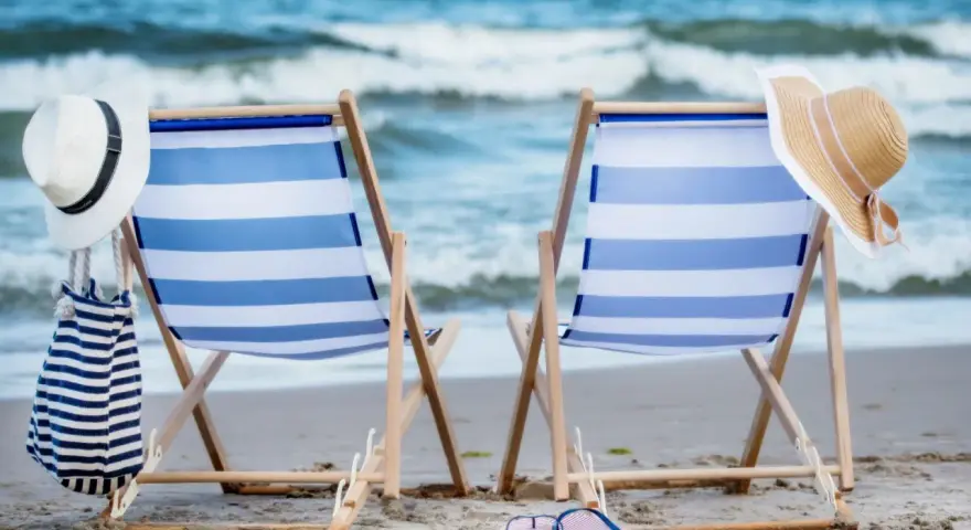 Dwa leżaki na plaży, gotowe na idealny weekend nad morzem. W tle szum fal i błękitne niebo.