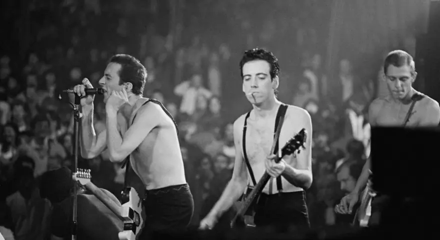 Le chanteur de The Clash, Joe Strummer, chante avec passion devant une foule en délire, guitare à la main.