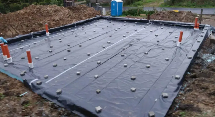 Fundament budowlany z folią i rurami. Widać małe kostki, które służą jako dystanse do zbrojenia, zapewniając odpowiednią grubość otuliny betonu.