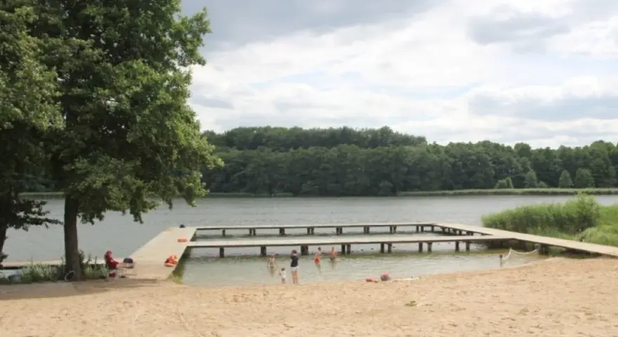 Plaża nad jeziorem Zaleskim z drewnianymi pomostami, na których bawią się ludzie.