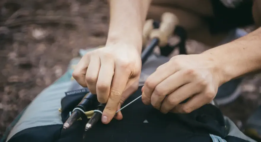 Ręce zapinają kijki trekkingowe do plecaka. Prosty sposób, jak przypiąć kijki do plecaka, by były zawsze pod ręką.