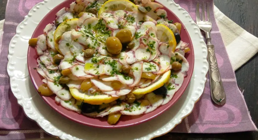 Carpaccio di polpo fresco, guarnito con olive, capperi e fette di limone, un piatto estivo da gustare.