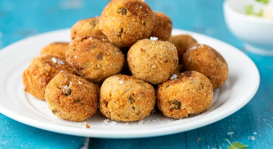 Pile di polpette tonno e ricotta dorate e croccanti, cosparse di sale grosso, su un piatto bianco.