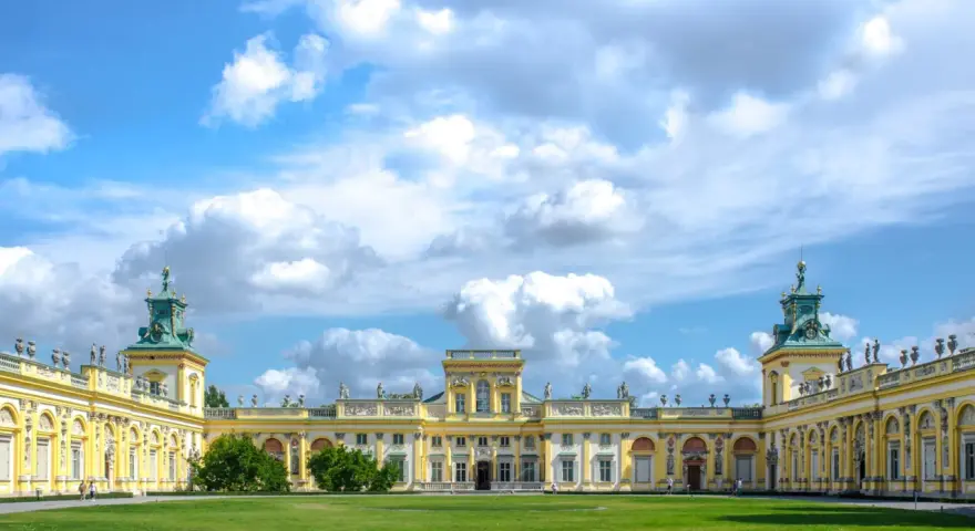 Pałac w Wilanowie zachwyca architekturą i ogrodami. Można zobaczyć bogato zdobione fasady, wieże i zielone trawniki.