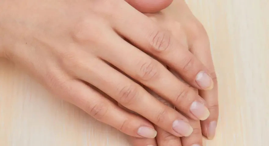 Mani curate, con unghie naturali e sane che sembrano respirare. La pelle è liscia e luminosa, poggiata su una superficie chiara.