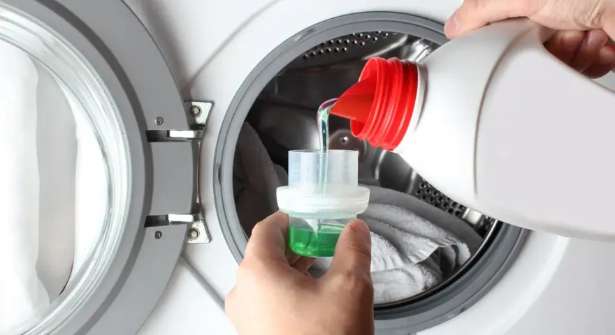 Versando detersivo liquido in un misurino per il prelavaggio lavatrice.