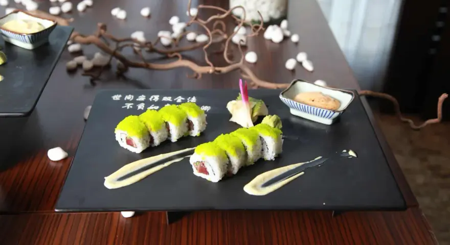 Dwa rzędy sushi z zielonym ikrą, podane z sosem i imbirem. Idealny sposób, jak podawać sushi na eleganckim talerzu.