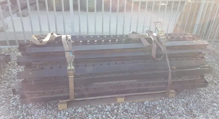 Stos czarnych, metalowych elementów naczepy z pasami transportowymi.