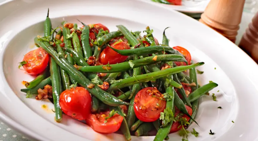 Insalata di fagiolini freschi con pomodorini ciliegino e erbe aromatiche, servita in un piatto bianco.