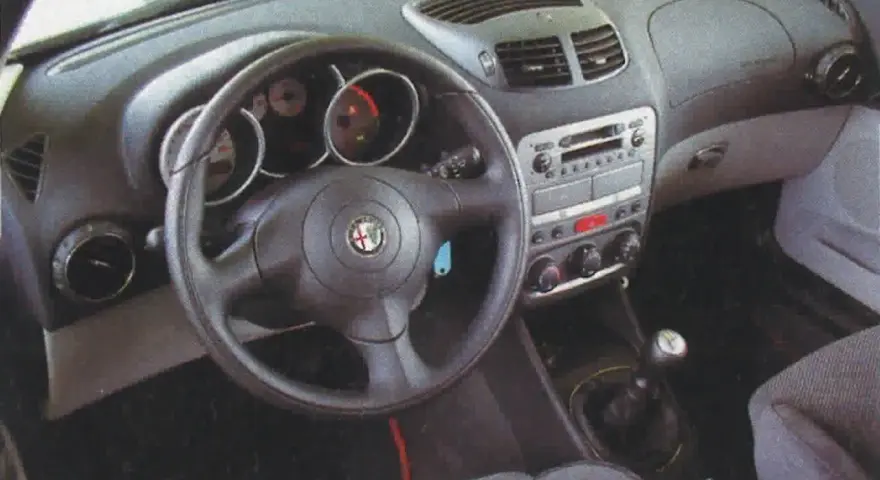 Wnętrze Alfa Romeo 147 1.9 JTD: kierownica, deska rozdzielcza z radiem i nawiewami, dźwignia zmiany biegów.