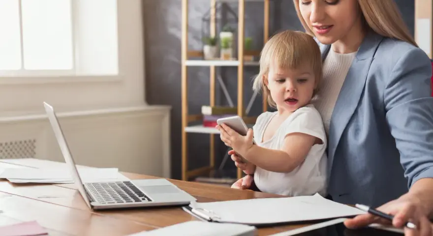 Praca na urlopie macierzyńskim? Młoda mama z dzieckiem przy biurku z laptopem i tabletem, pokazująca, że można łączyć obowiązki.